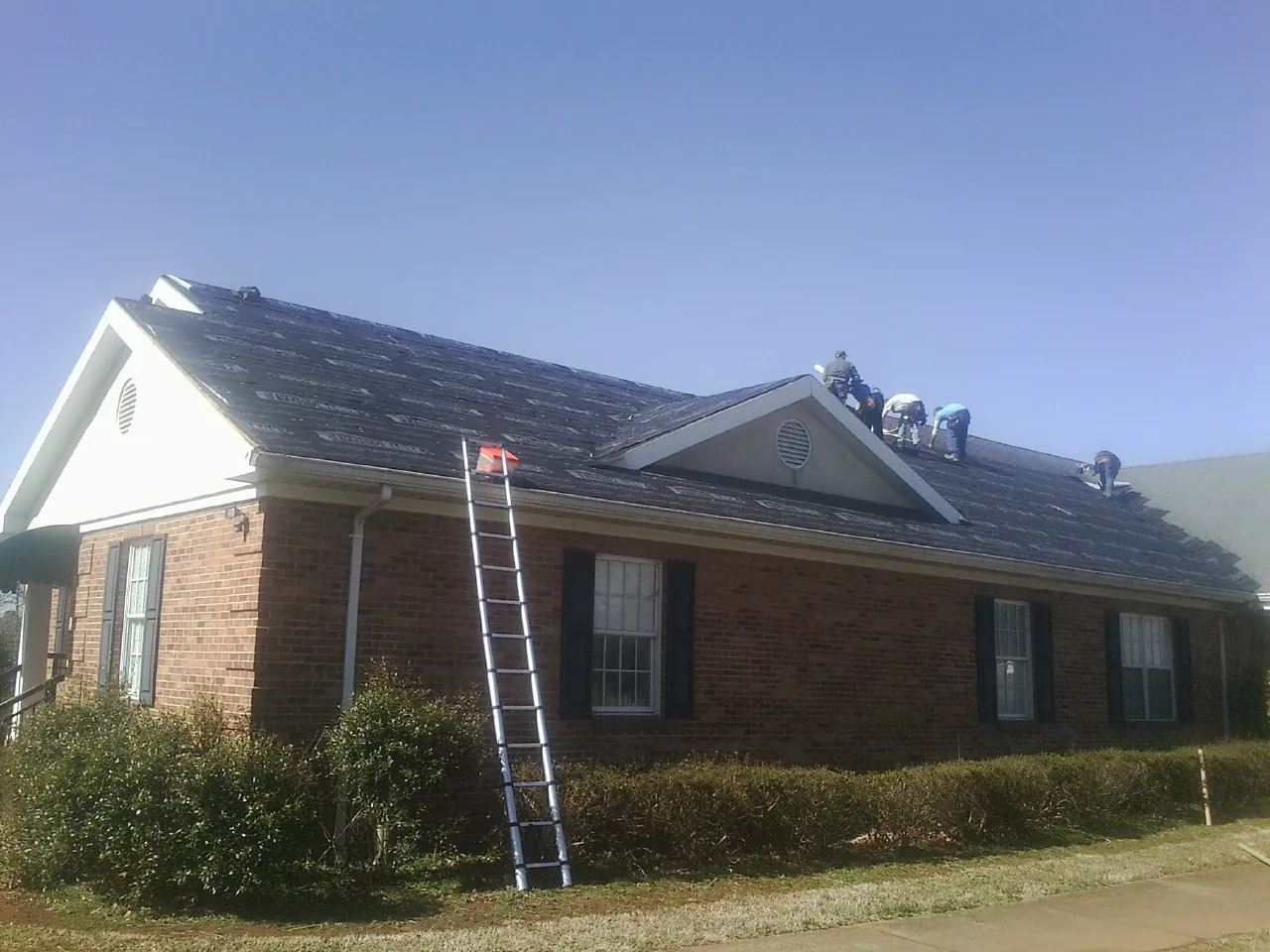 Crew tearing shingles off a brick ranch roof with a ladder set — Emergency Roof Repair work by our crew in Creola