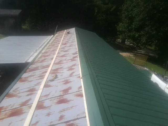 Old rusted panels beside newly installed green metal roofing — Wind Damage Roof Repair by Roofing Brothers in Creola
