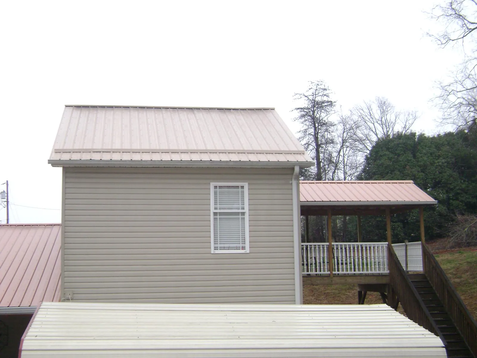 Tan metal roofs on a two story addition and attached porch, from a Roof Replacement job in Creola